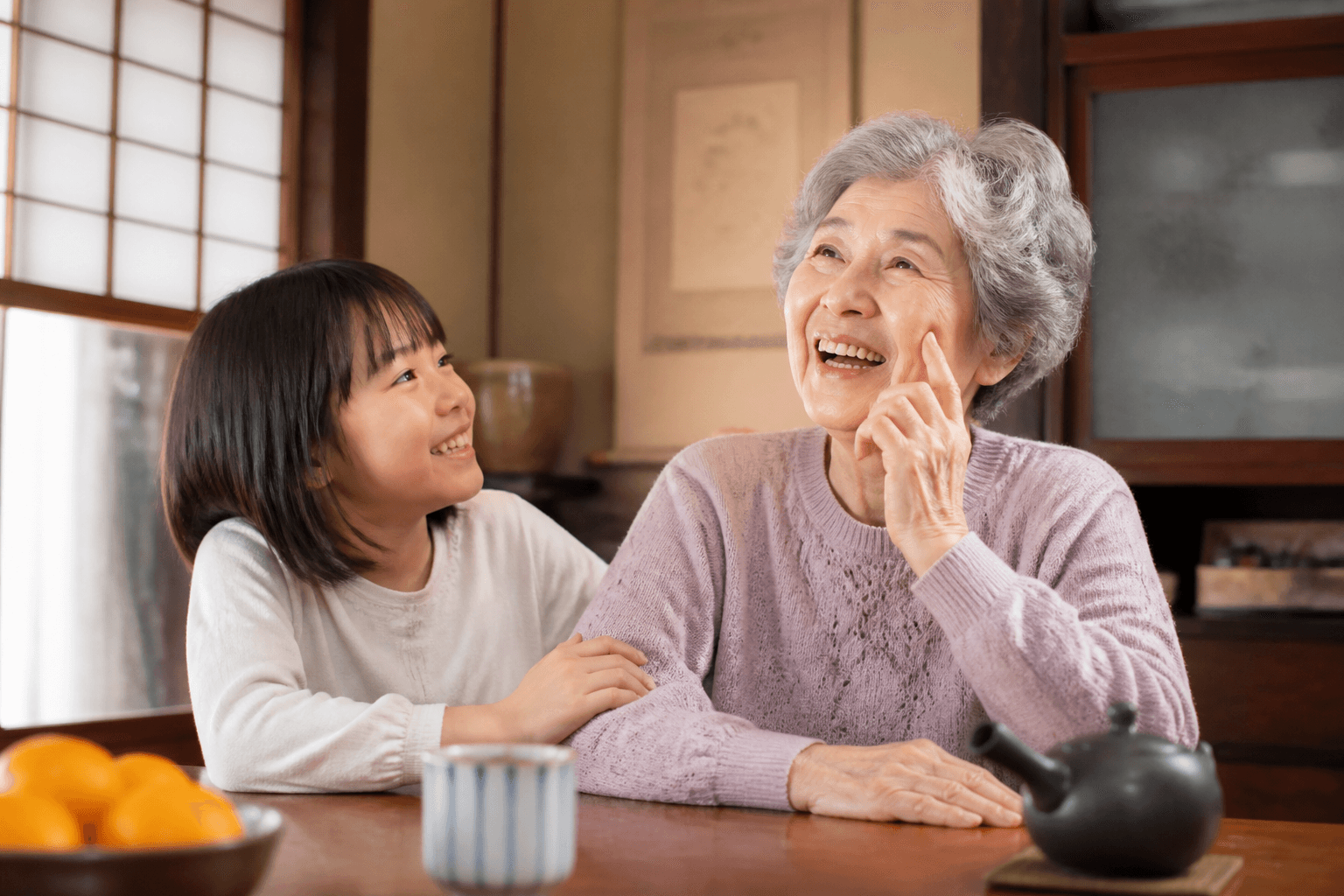 孫が祖母に優しく話しかけ、祖母が笑顔で昔を思い出している様子の写真。温かい雰囲気で。]