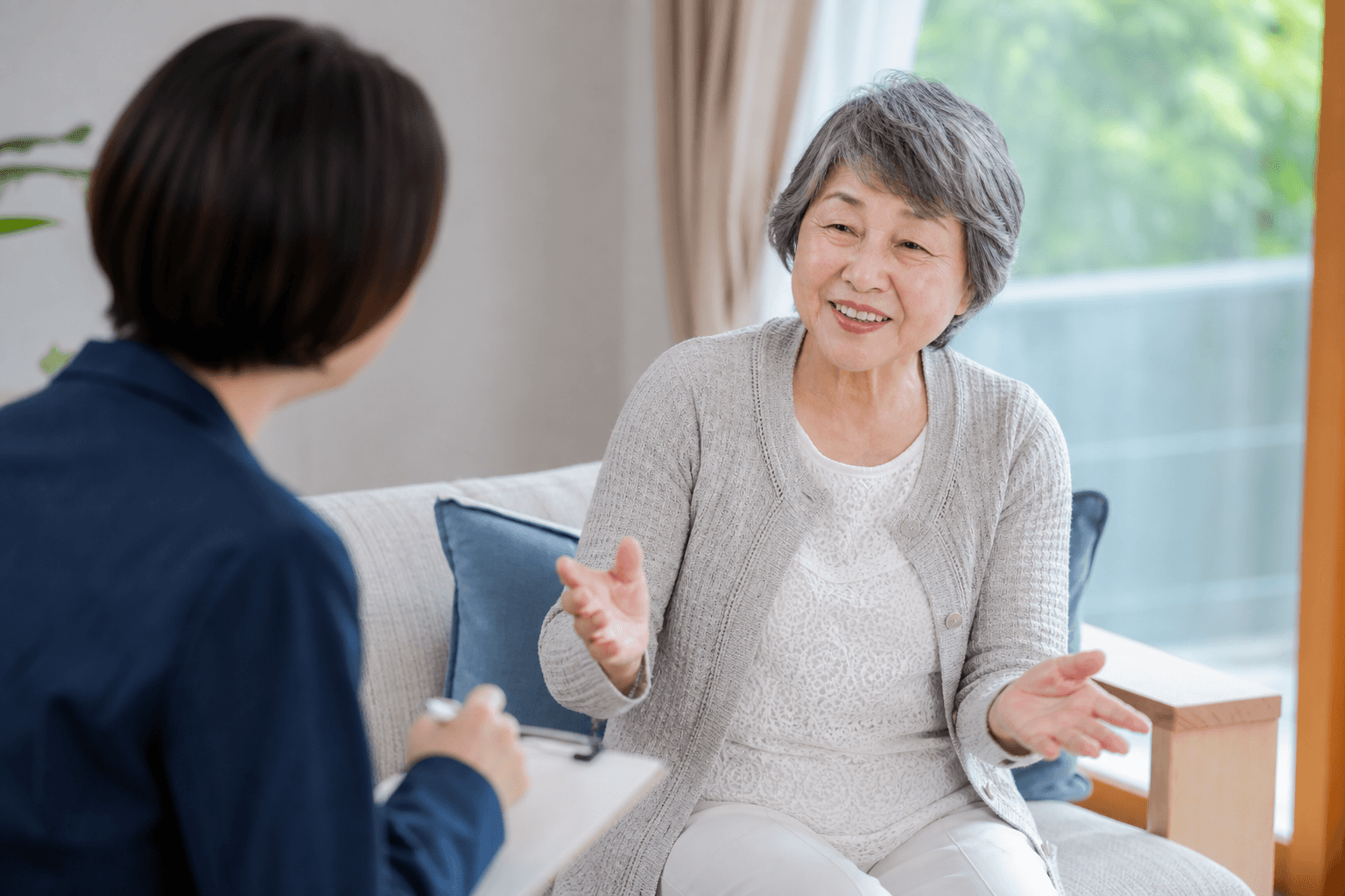 高齢のお客様がご自宅のリビングなどで、リラックスしながら編集者と楽しそうにお話をしている取材風景の写真。聞き手は真摯に耳を傾けている様子が伝わるもの。]